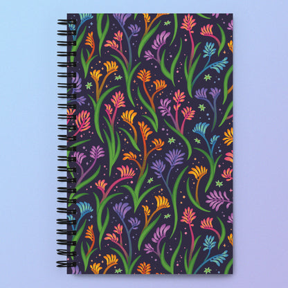 Spiral notebook with a colourful rainbow kangaroo paw flower pattern on a pink and purple gradient background.