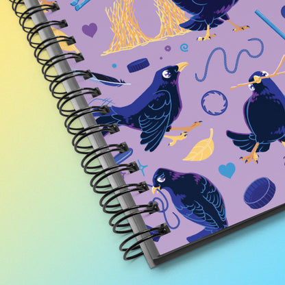 Close up of a spiral notebook with a colourful purple, blue and yellow satin bowerbird pattern on a yellow and blue gradient background.
