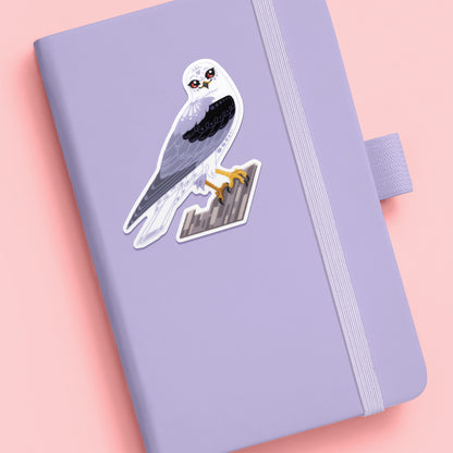 Colourful sticker of a black-shouldered kite perched on a branch stuck to a pale lilac journal on an soft pink background.