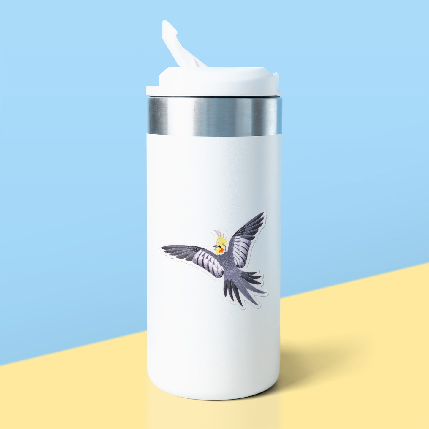 Colourful sticker of a male wild-type cockatiel spreading his wings wide stuck to a white metal drink bottle on a yellow table on a blue background.