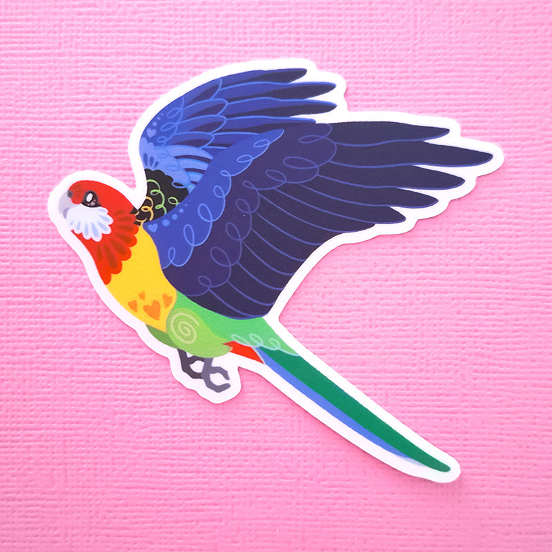 Real photo of a colourful sticker of an Eastern Rosella in flight on a pink canvas textured background.