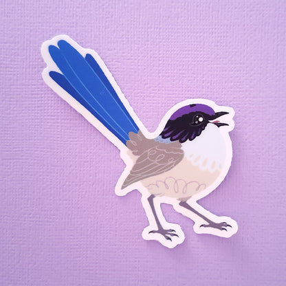 Real photo of a colourful sticker of a male Purple-Crowned Fairywren chirping on a purple canvas textured background.