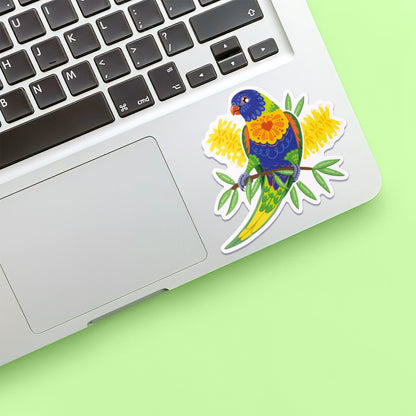 Colourful sticker of a rainbow lorikeet with yellow bottlebrush flowers stuck below the keyboard of a Macbook laptop on a green background.