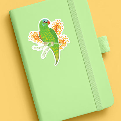 A colourful sticker of a scaly-breasted lorikeet with orange grevillea flowers stuck to a pale green journal on a yellow background.