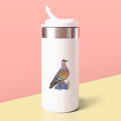 Colourful die-cut sticker of a male common bronzewing pigeon stuck to a white metal drink bottle on a soft yellow table on a peach background.