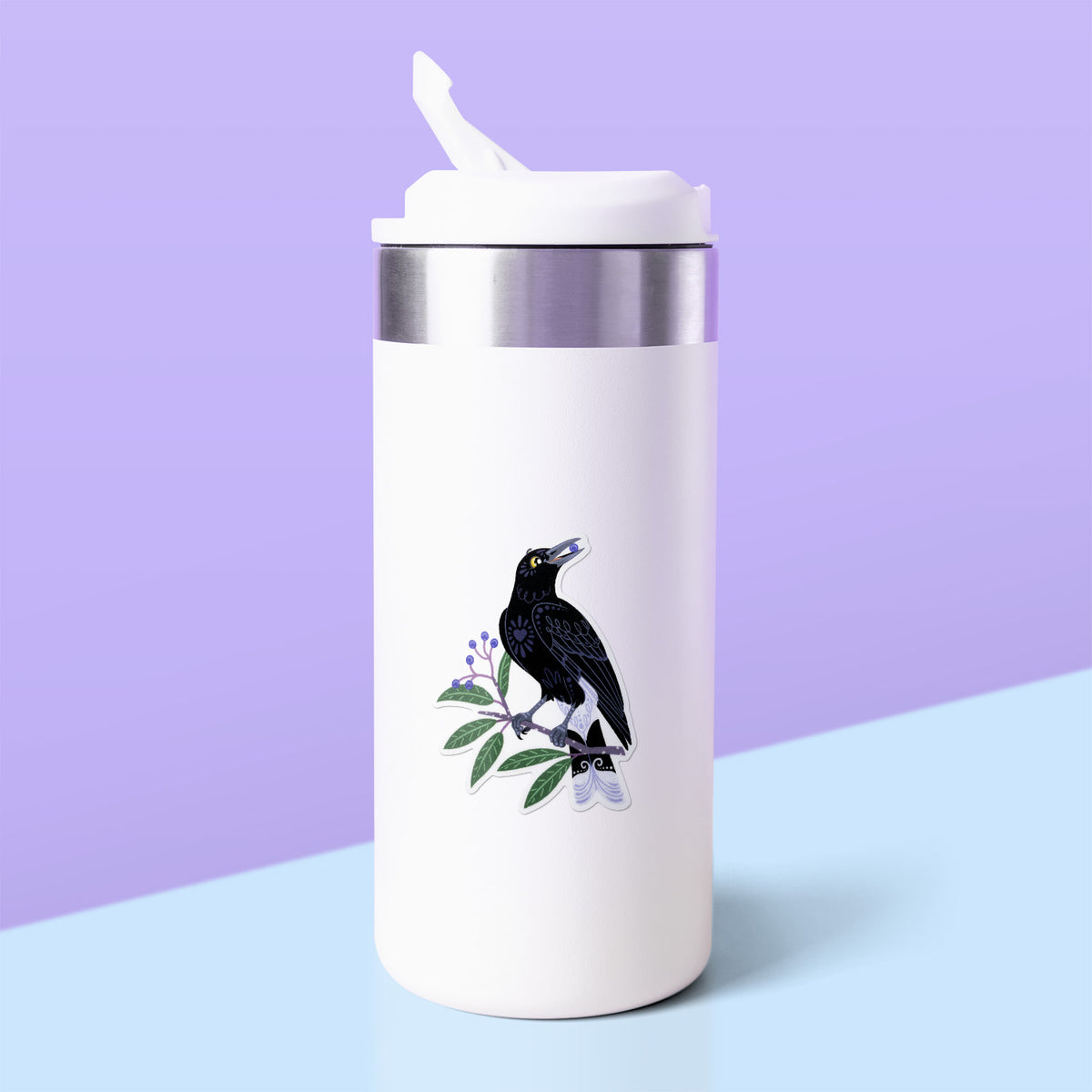 Colourful diecut sticker of a pied currawong eating a blueberry ash berry stuck to a white metal drink bottle on a soft blue table on a purple background.