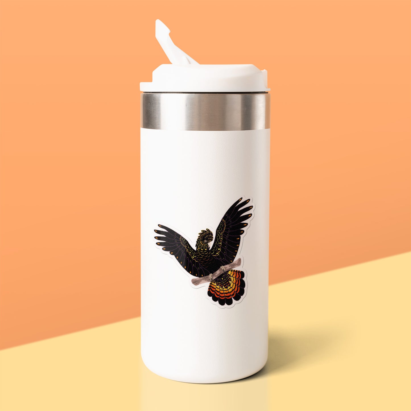 Colourful sticker of a female red-tailed black cockatoo perched on a branch with her wings out stuck to a white metal drink bottle on a yellow table on an orange background.