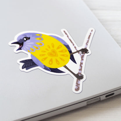 Closeup of a colourful sticker of an eastern yellow robin perched on a lichen-covered branch stuck to a lid of a Macbook laptop on a textured white wood background.