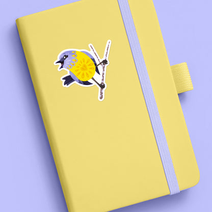 Colourful sticker of an eastern yellow robin perched on a lichen-covered branch stuck to a pale yellow journal on a lilac background.