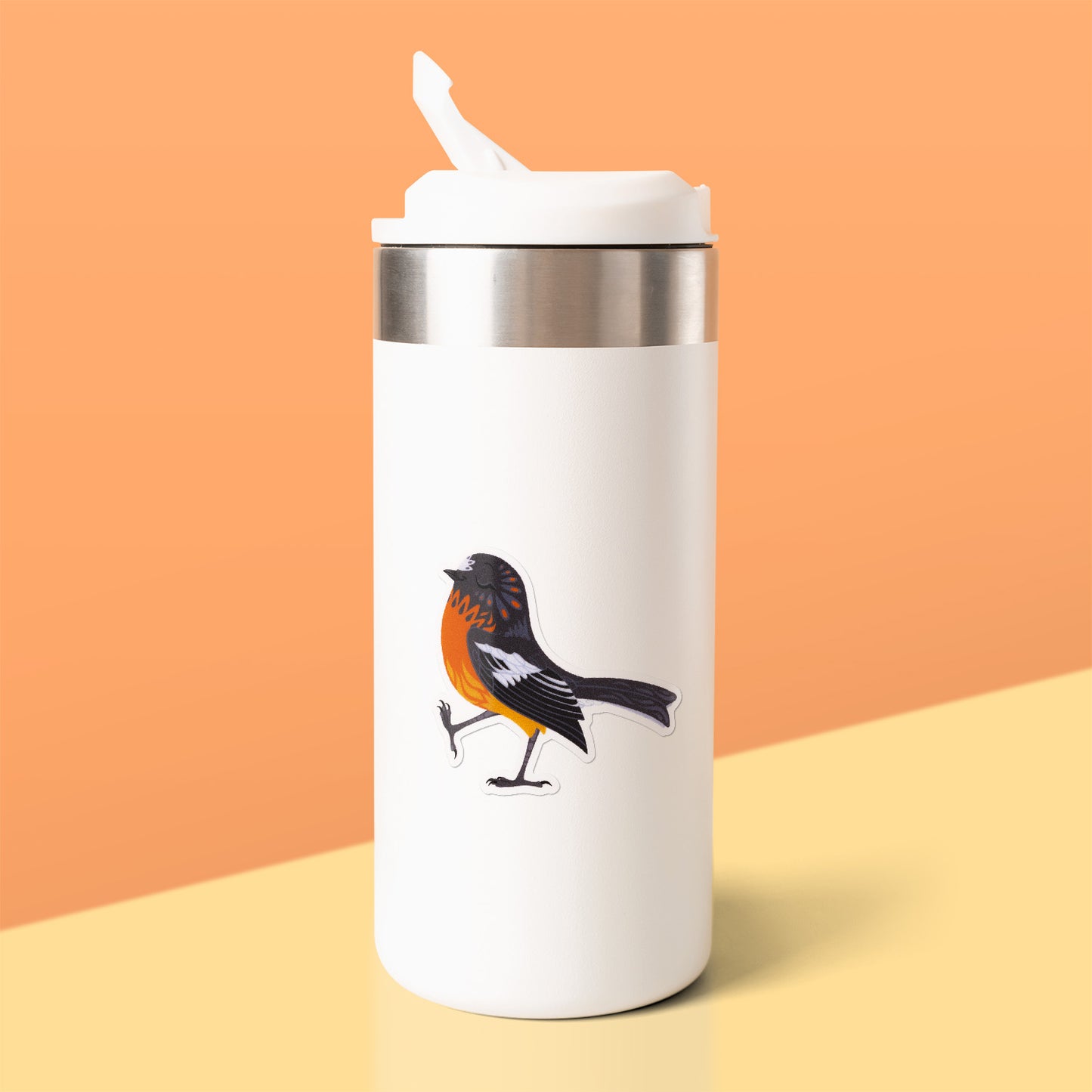Colourful sticker of a male flame robin walking with pep in his step stuck to a white metal drink bottle on a yellow table on an orange background.