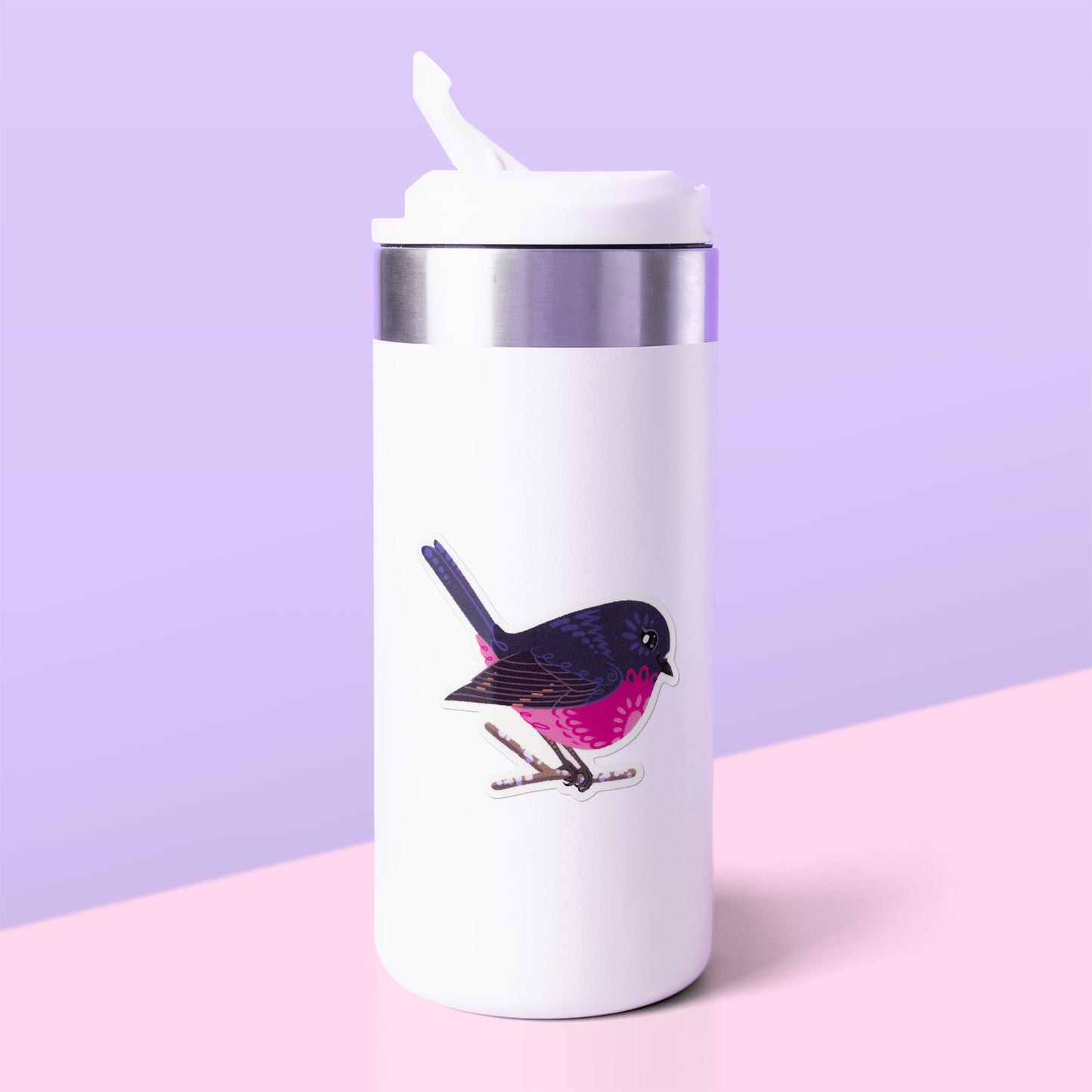 Colourful sticker of a male pink robin perched on a lichen-covered branch stuck to a white metal drink bottle on a light pink table on a lilac background.