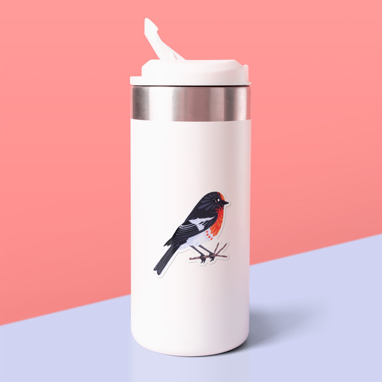 Colourful sticker of a male red-capped robin perched on a lichen-covered branch stuck to a white metal drink bottle on a grey table on a rose pink background.