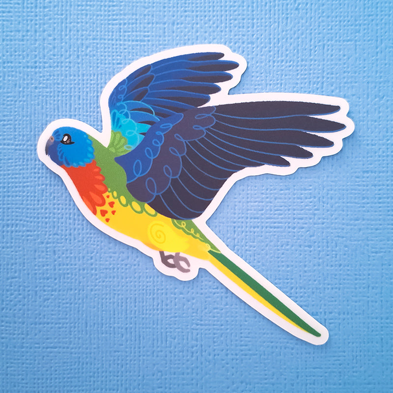 Real photo of a colourful sticker of a Scarlet-Chested Parrot in flight on a blue canvas textured background.