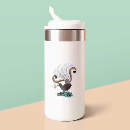 Colourful sticker of a male superb lyrebird singing stuck to a white metal drink bottle on a beige table on a pale green background.