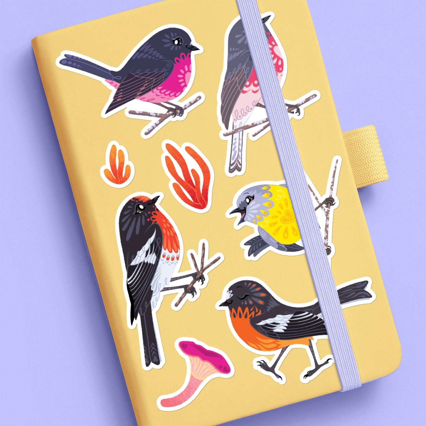 Assorted colourful red/pink/orange/black Australian robin, lichen and fungi stickers stuck to a pale yellow journal on a lilac background.