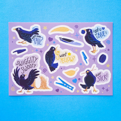Real photo of a colourful A5 sticker sheet of 5 different male Satin Bowerbirds, yellow leaves, blue feathers, pen caps, bottle caps and pegs on a blue canvas texture background.