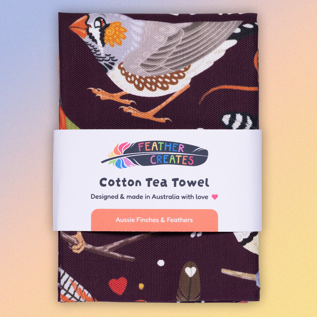 A folded tea towel with a burgundy Australian finches pattern sitting flat on a pastel blue, orange and yellow background.