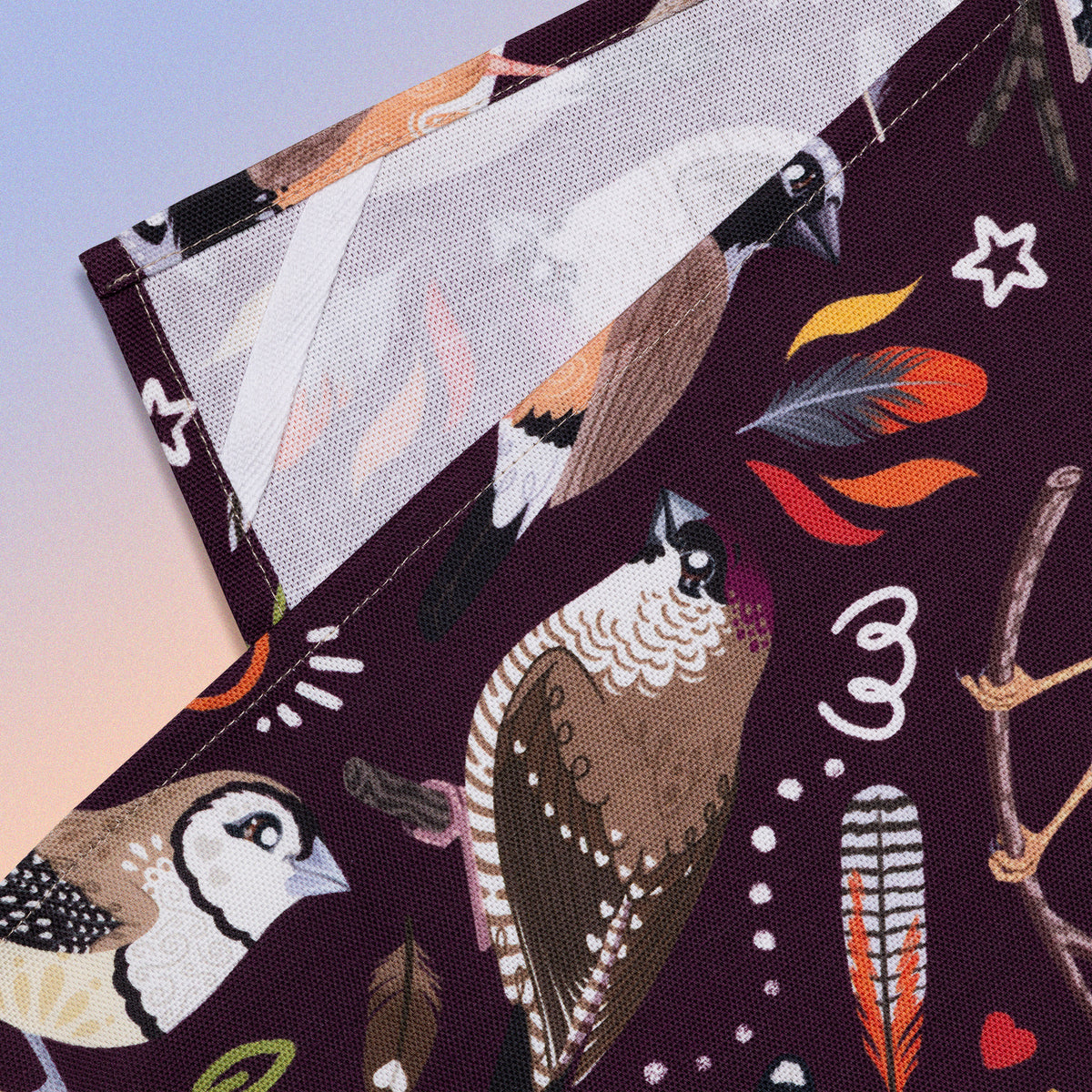 Closeup of a hanging strap on the reverse side of a tea towel with a burgundy Australian finches pattern sitting flat on a pastel blue, orange and yellow background.