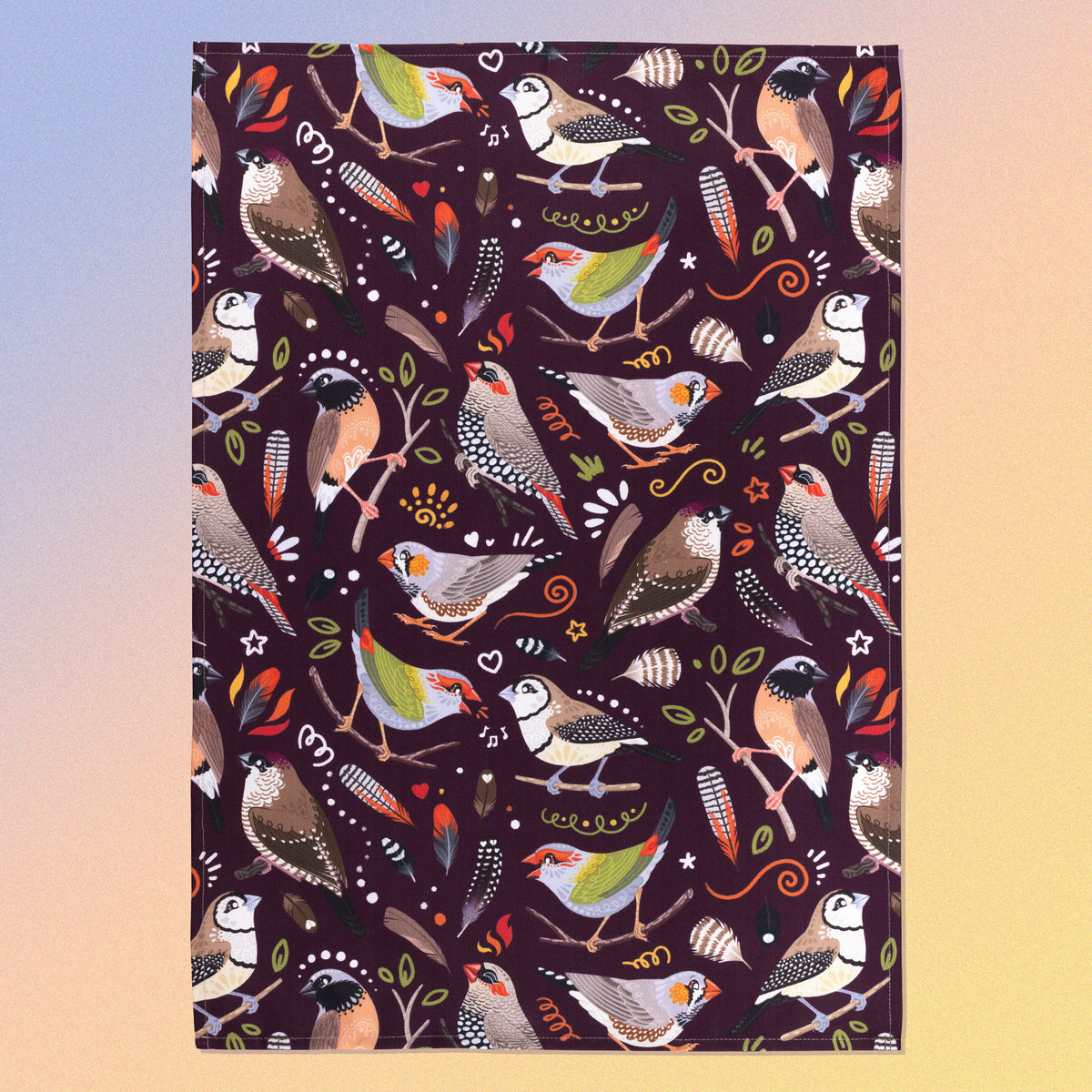 A tea towel with a burgundy Australian finches pattern sitting flat on a pastel blue, orange and yellow background.