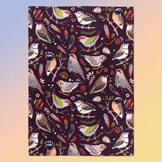 A tea towel with a burgundy Australian finches pattern sitting flat on a pastel blue, orange and yellow background.