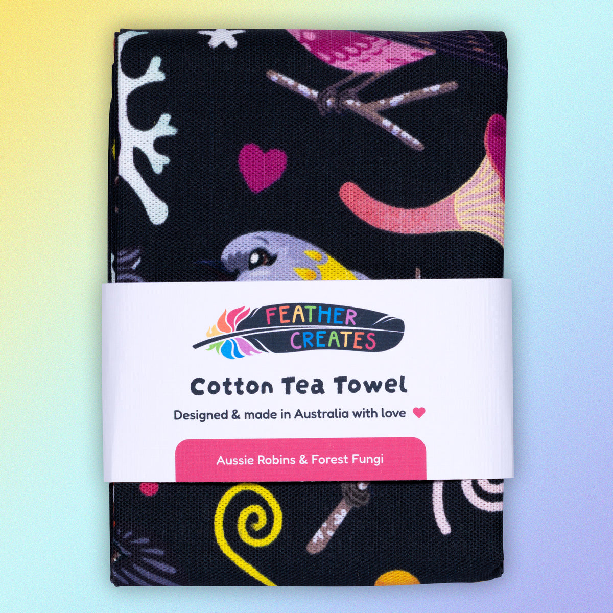 A folded tea towel with a black, pink, orange and yellow Australian robins pattern sitting flat on a pastel yellow and lilac background.