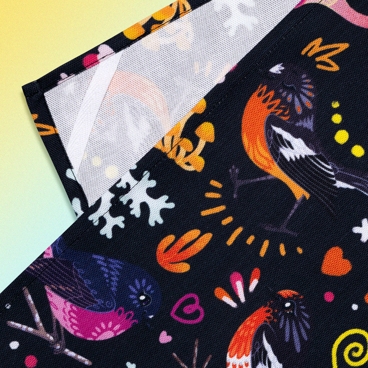 Closeup of a hanging strap on the reverse side of a tea towel with a black, pink, orange and yellow Australian robins pattern sitting flat on a pastel yellow and lilac background.