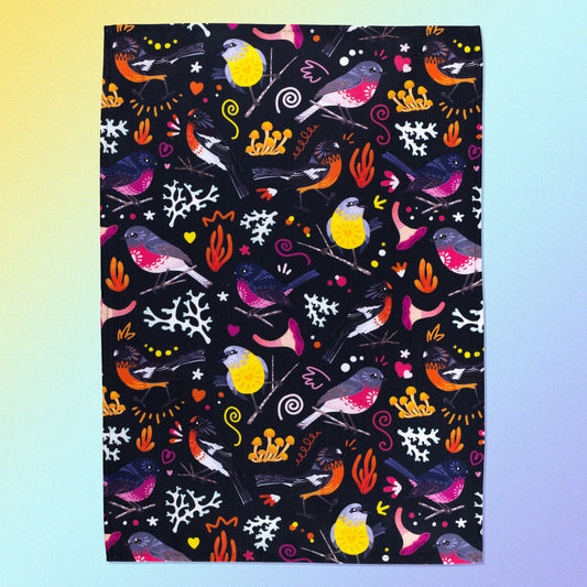 A tea towel with a black, pink, orange and yellow Australian robins pattern sitting flat on a pastel yellow and lilac background.