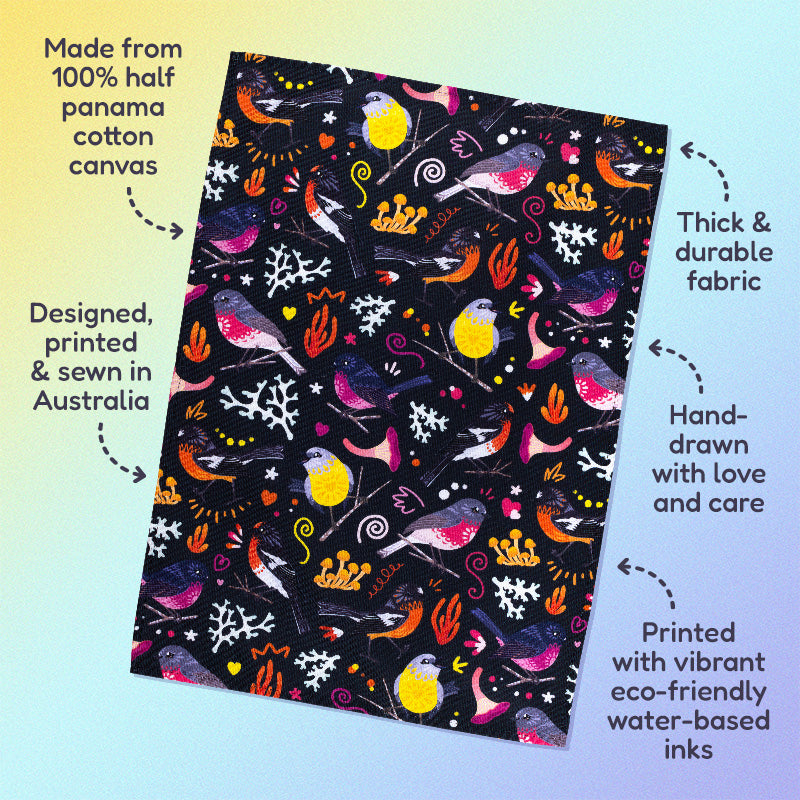 Features & benefits ('Made from 100% half panama cotton canvas, designed, printed & sewn in Australia, thick & durable fabric, hand-drawn with love and care, printed with vibrant eco-friendly water-based inks) surrounding a tea towel with a black, pink, orange and yellow Australian robins pattern sitting flat on a pastel yellow and lilac background.