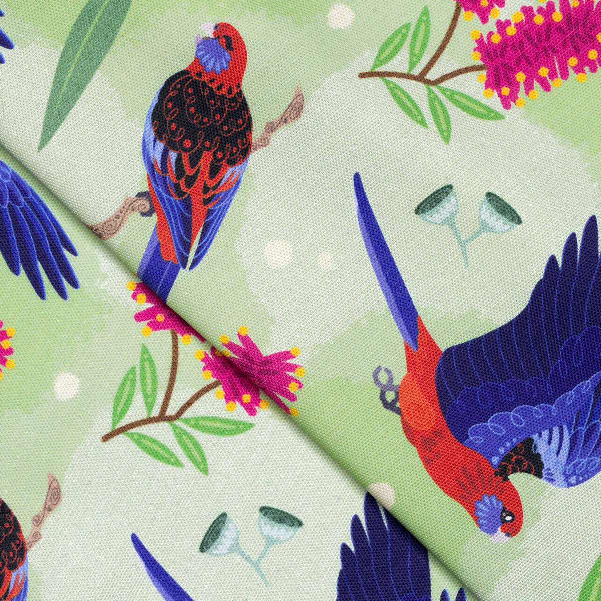 Closeup of a folded tea towel with a green, red and blue crimson rosellas pattern.