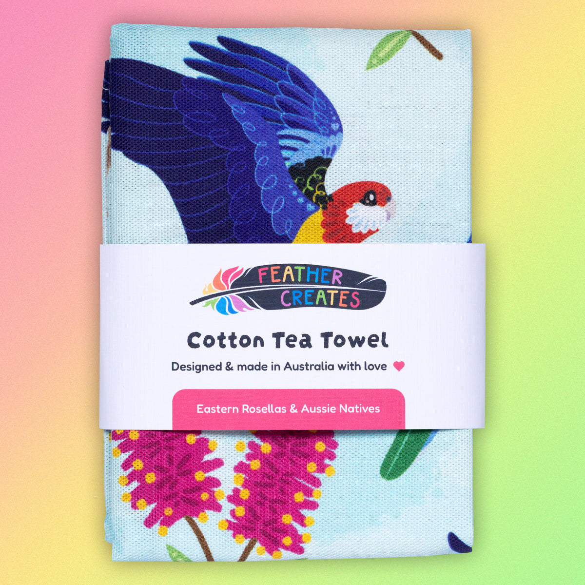 A folded tea towel with a rainbow eastern rosellas pattern sitting flat on a pastel pink, yellow and green background.