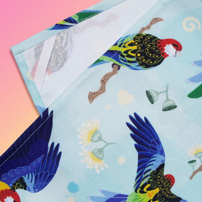 Closeup of a hanging strap on the reverse side of a tea towel with a rainbow eastern rosellas pattern sitting flat on a pastel pink, yellow and green background.
