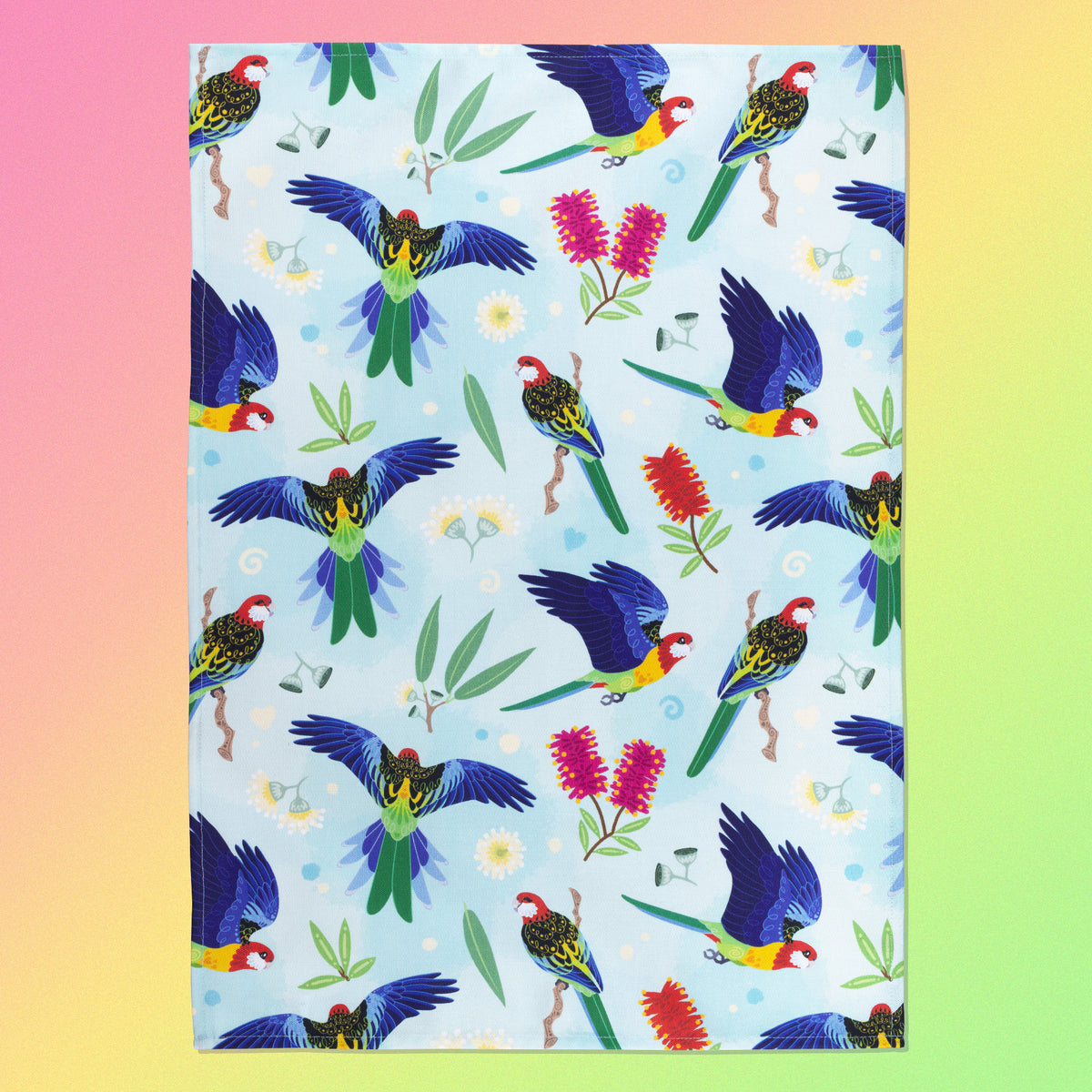 A tea towel with a rainbow eastern rosellas pattern sitting flat on a pastel pink, yellow and green background.