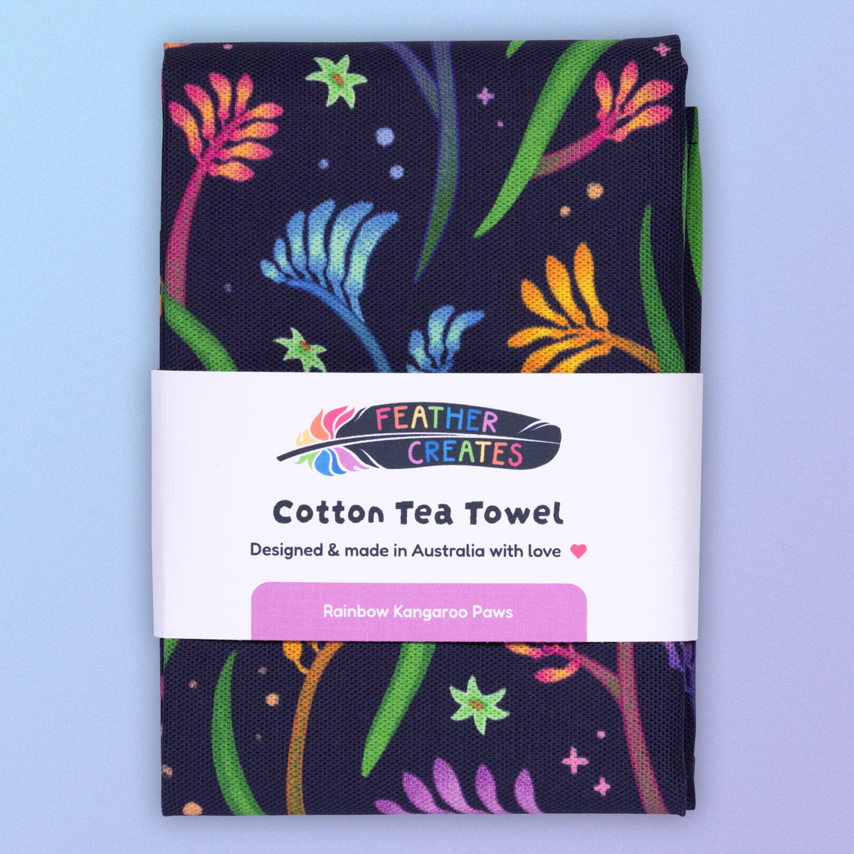 A folded tea towel with a rainbow kangaroo paw pattern sitting on a pastel blue and purple background.