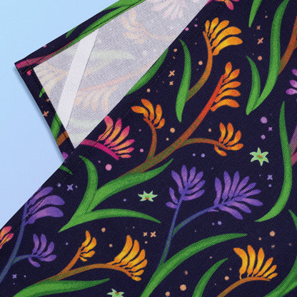 Closeup of a hanging strap on the reverse side of a tea towel with a rainbow kangaroo paw pattern sitting on a pastel blue and purple background.