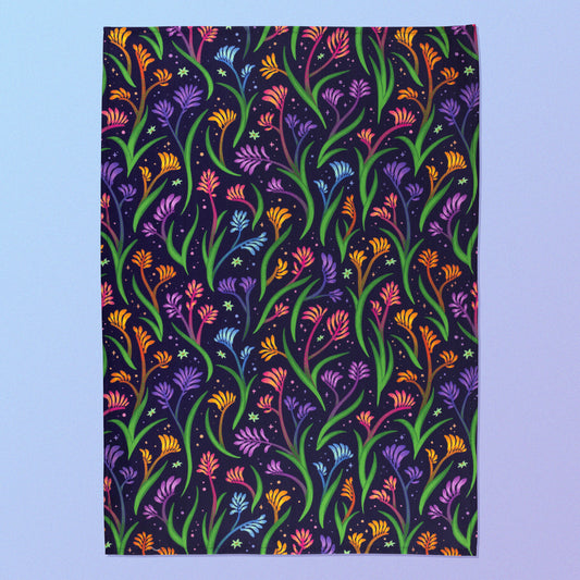A tea towel with a rainbow kangaroo paw pattern sitting on a pastel blue and purple background.