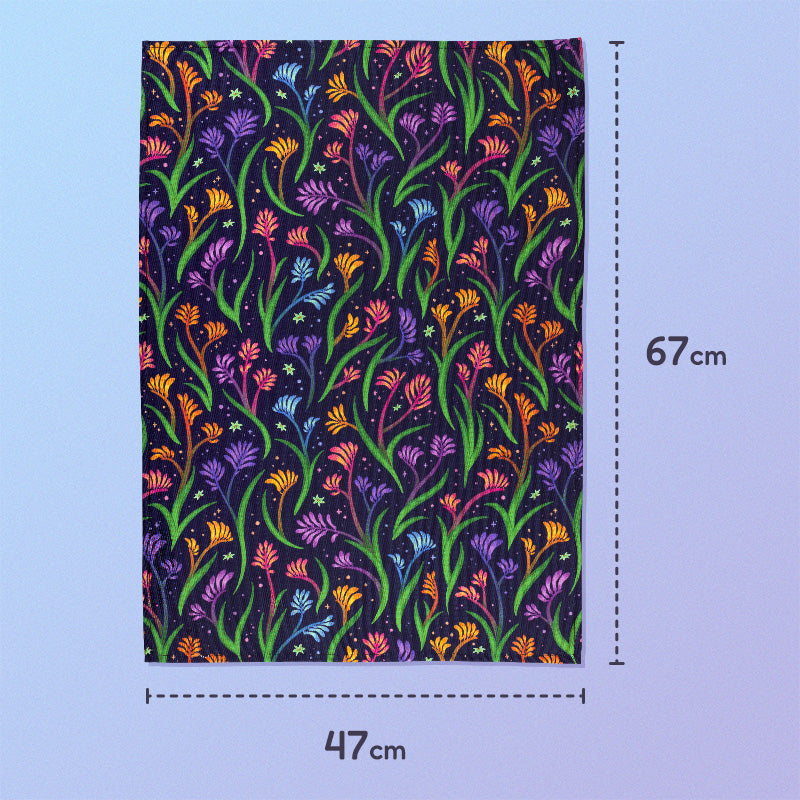 47x67cm tea towel with a rainbow kangaroo paw pattern sitting on a pastel blue and purple background.