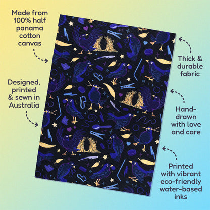 Features & benefits ('Made from 100% half panama cotton canvas, designed, printed & sewn in Australia, thick & durable fabric, hand-drawn with love and care, printed with vibrant eco-friendly water-based inks) surrounding a tea towel with a black, blue, purple and yellow satin bowerbirds pattern sitting flat on a pastel yellow and blue background.