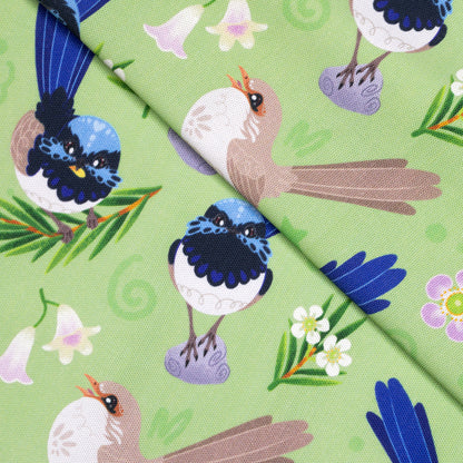 Closeup of a folded tea towel with a green, blue, yellow and beige superb fairywrens pattern.