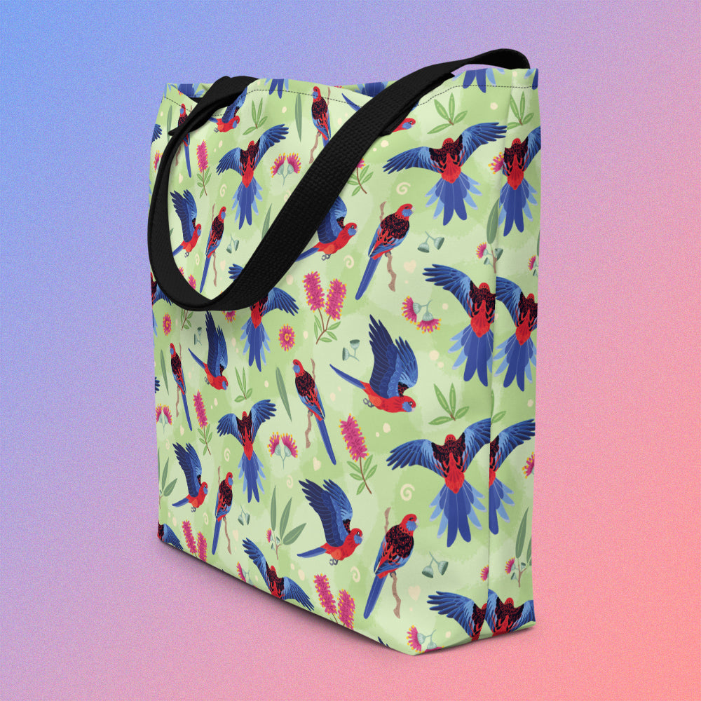 Tote bag on an angle with black handles and a crimson rosella parrot pattern on a gradient purple and pink background