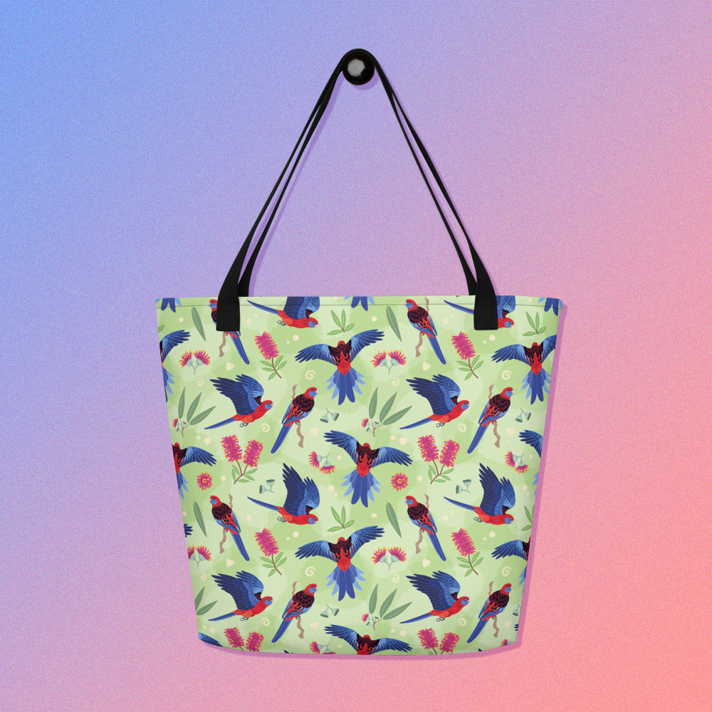 Tote bag with black handles and a crimson rosella parrot pattern on a gradient purple and pink background