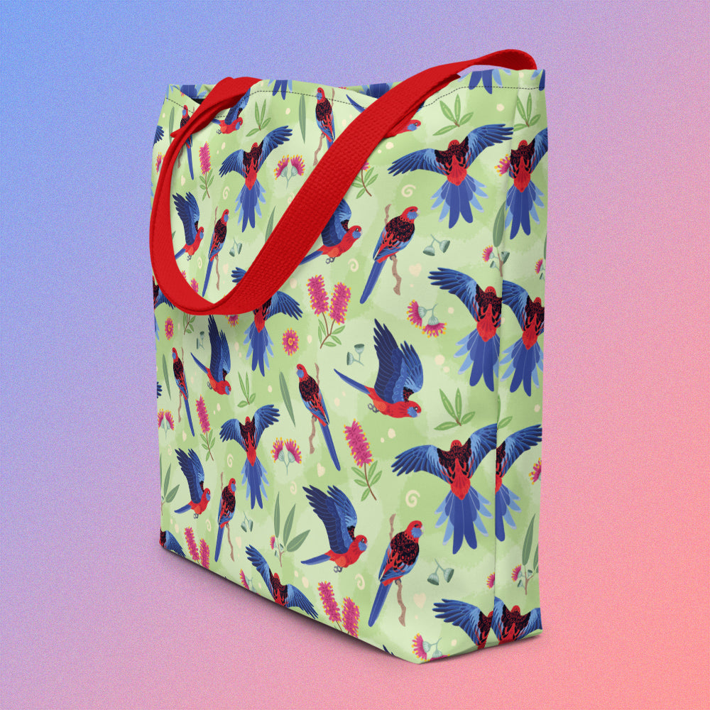 Tote bag on an angle with red handles and a crimson rosella parrot pattern on a gradient purple and pink background