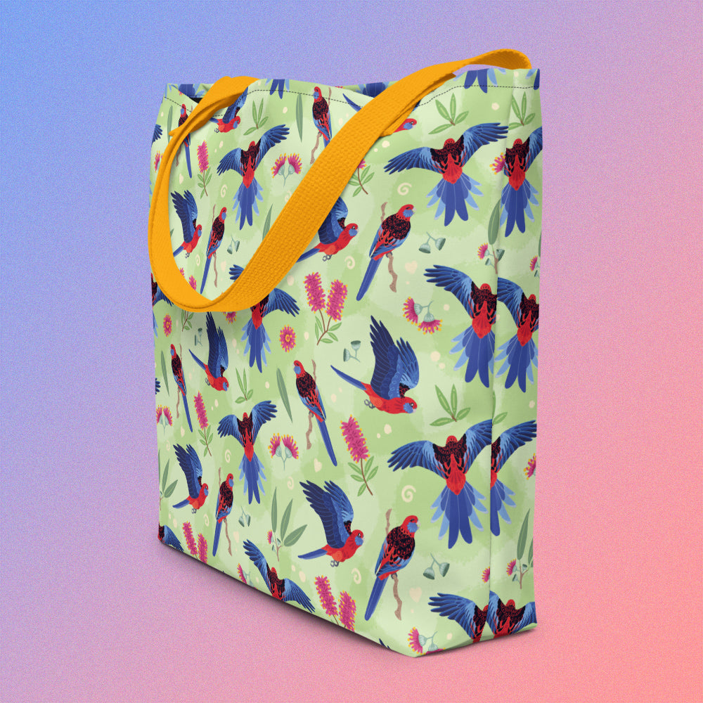 Tote bag on an angle with yellow handles and a crimson rosella parrot pattern on a gradient purple and pink background