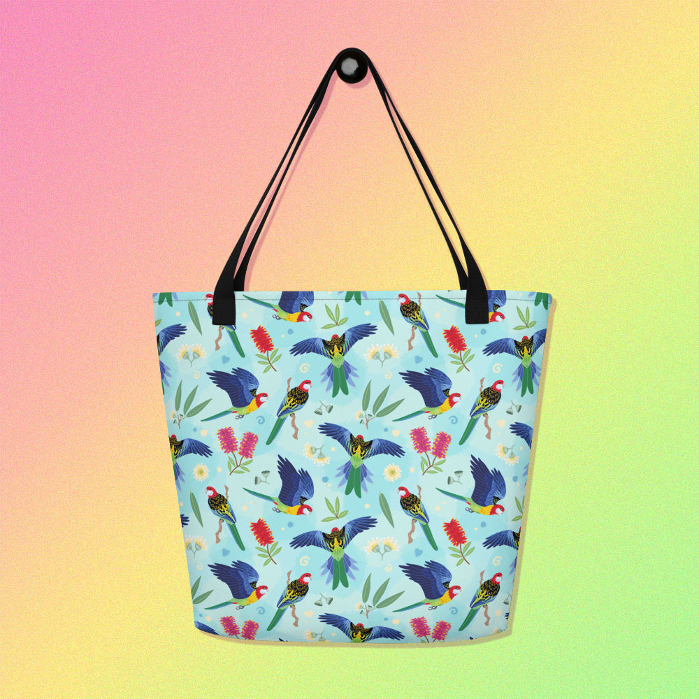 Tote bag with black handles and an eastern rosella parrot pattern on a gradient pink, yellow and green background.