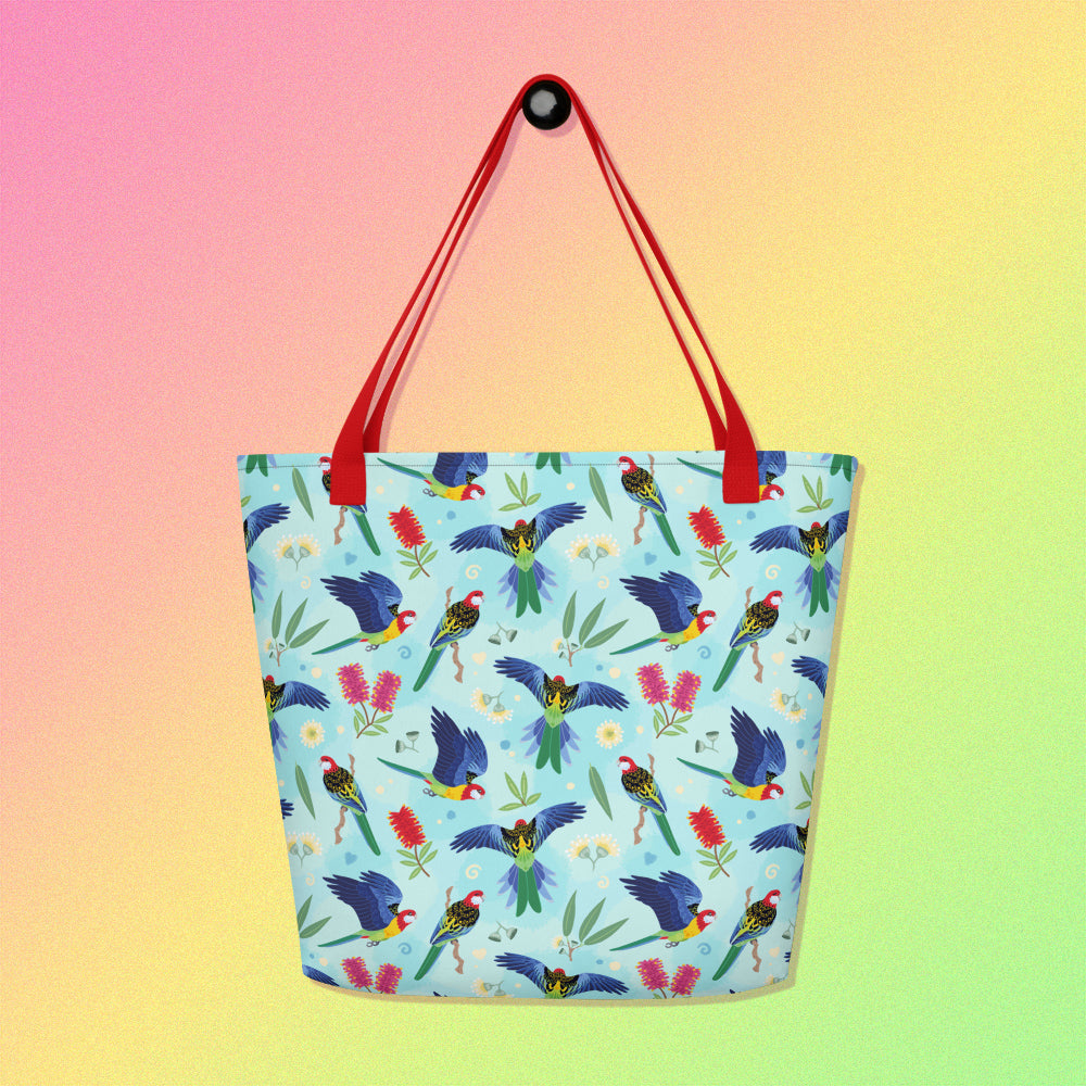 Tote bag with red handles and an eastern rosella parrot pattern on a gradient pink, yellow and green background.