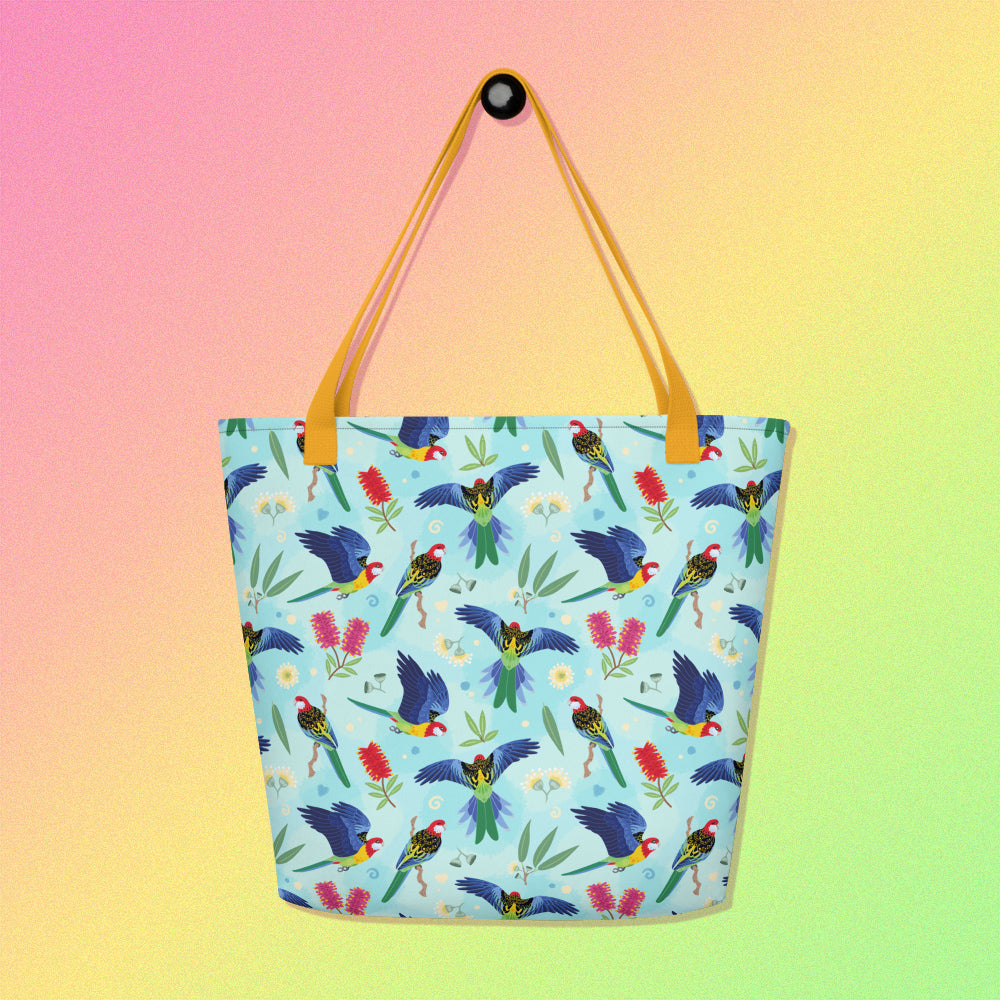 Tote bag with yellow handles and an eastern rosella parrot pattern on a gradient pink, yellow and green background.