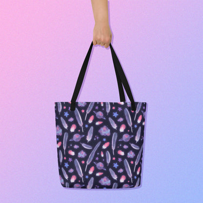 Hand holding a tote bag from above with a black strap and galah cockatoo feather and galaxy-themed pattern on a gradient purple background.