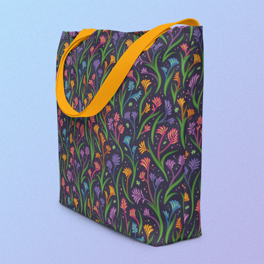 Tote bag on an angle with a yellow strap and a floral rainbow kangaroo paw pattern on a gradient blue and purple background.