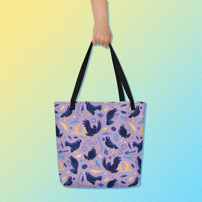 Hand holding a tote bag with black handles and a purple/blue/yellow satin bowerbird pattern on a yellow and blue gradient background.