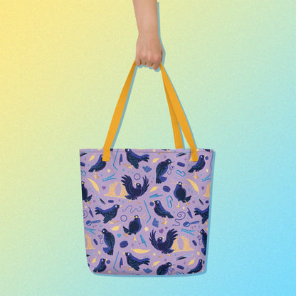 Hand holding a tote bag with yellow handles and a purple/blue/yellow satin bowerbird pattern on a yellow and blue gradient background.