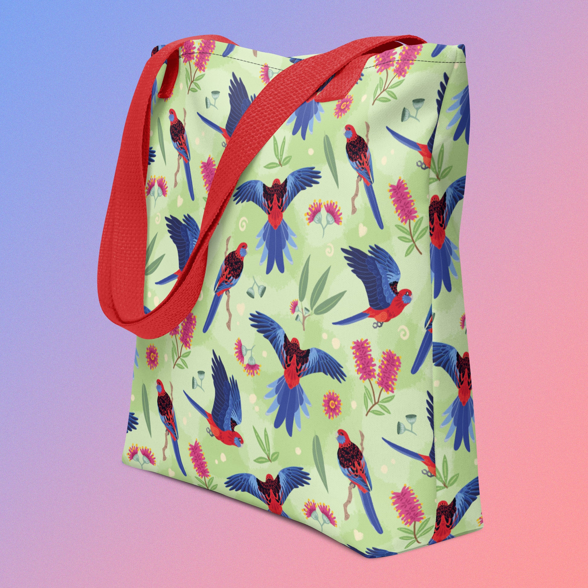 Tote bag with red handles and a crimson rosella parrot pattern on an angle on a gradient purple and pink background